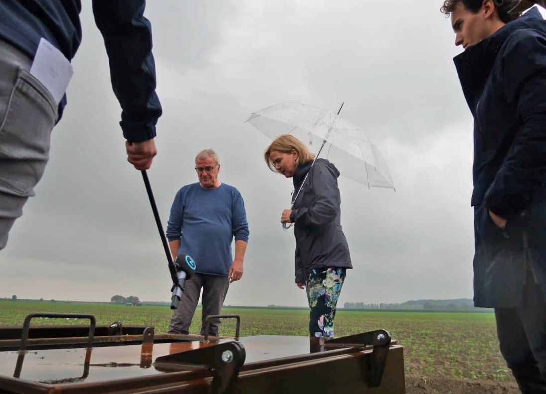 Op gepaste afstand van 1,5 meter wegens coronamaatregelen krijgt minister Van Nieuwenhuizen te midden van de wortelen toelichting over peilgestuurde drainage en ondergrondse waterberging (links: Alex van Hootegem van Meulwaeter, rechts: Teun van Dooren van KWR).